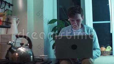 年轻人坐在厨房里打电脑，一边烧水壶